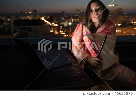 Girl sits wrapped in a blanket and smokes a hookah. 45625876