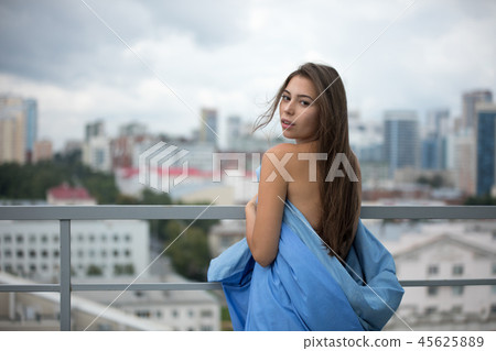 Naked girl wrapped in a blanket stands on the terrace overlooking the city. 45625889