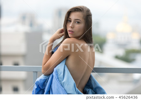 Naked girl wrapped in a blanket stands on the terrace overlooking the city. Naked girl wrapped in a blanket stands on the terrace overlooking the city. 45626436