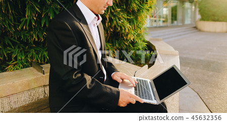 Businessman working with laptop outside near plant in  . 45632356
