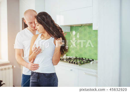 Beautiful young couple is talking, looking at camera and smiling while cooking in kitchen. Beautiful young couple is talking, looking at camera and smiling while cooking in kitchen. 45632920