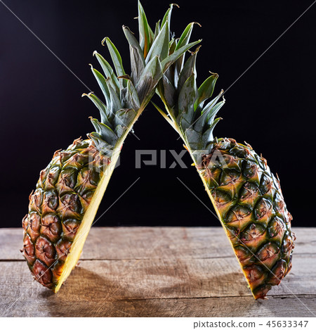 Tropical ripe fruit pineapple with green leaves presented on a wooden table around a dark background Tropical ripe fruit pineapple with green leaves presented on a wooden table around a dark background 45633347