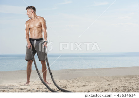Young man training with battle ropes on the beach Young man training with battle ropes on the beach 45634634