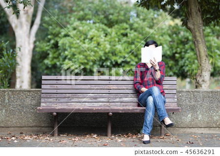 A woman reading a book on a park bench 45636291