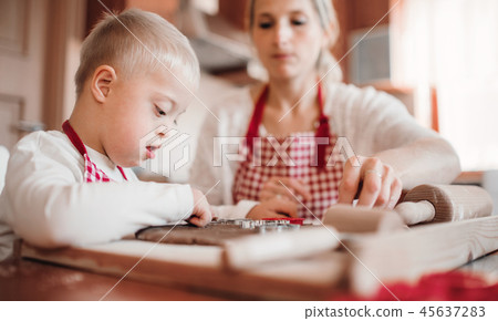 A handicapped down syndrome boy with his mother indoors baking. A handicapped down syndrome boy with his mother indoors baking. 45637283