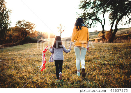 Rear view of young mother with a small daughter walking in autumn nature at sunset. Rear view of young mother with a small daughter walking in autumn nature at sunset. 45637375
