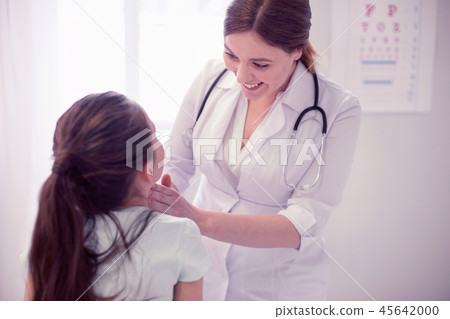 Smiling caring family physician exploring throat of little girl 45642000