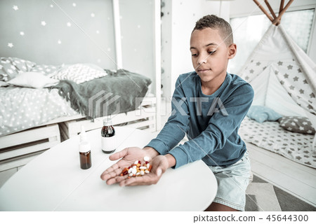Cheerless ill boy holding a handful of pills 45644300