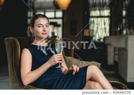Fashionable gorgeous girl in a dark blue dress drinking cocktail in a luxery hotel lobby bar Fashionable gorgeous girl in a dark blue dress drinking cocktail in a luxery hotel lobby bar 45646576