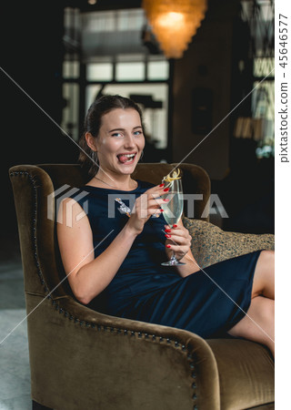 Fashionable gorgeous girl in a dark blue dress drinking cocktail in a luxery hotel lobby bar Fashionable gorgeous girl in a dark blue dress drinking cocktail in a luxery hotel lobby bar 45646577