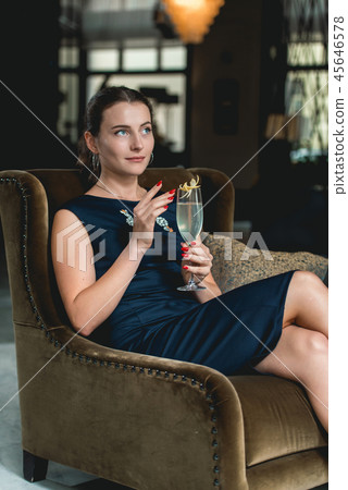 Fashionable gorgeous girl in a dark blue dress drinking cocktail in a luxery hotel lobby bar Fashionable gorgeous girl in a dark blue dress drinking cocktail in a luxery hotel lobby bar 45646578