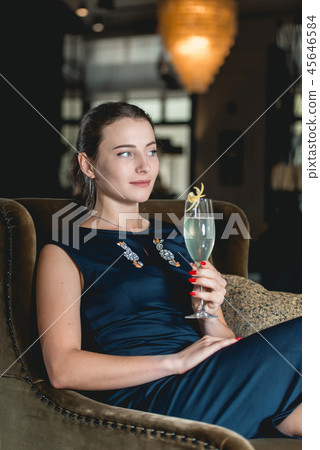 Fashionable gorgeous girl in a dark blue dress drinking cocktail in a luxery hotel lobby bar Fashionable gorgeous girl in a dark blue dress drinking cocktail in a luxery hotel lobby bar 45646584