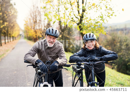 Active senior couple with electrobikes standing outdoors on a road in nature. Active senior couple with electrobikes standing outdoors on a road in nature. 45663711