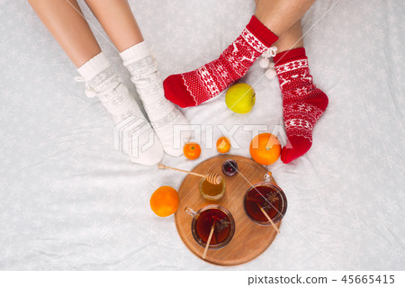 Soft photo of woman and man on the bed with tea and fruits, top view point. Female and male legs in Soft photo of woman and man on the bed with tea and fruits, top view point. Female and male legs in 45665415