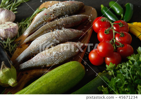 fresh raw dorada fish on a wooden board with a set of vegetables on a black table fresh raw dorada fish on a wooden board with a set of vegetables on a black table 45671234