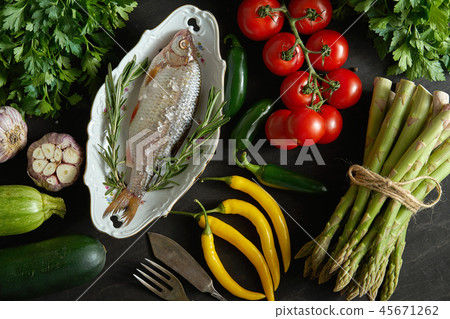 top view of fresh raw dorada fish in a white dish with a set of vegetables on a black table top view of fresh raw dorada fish in a white dish with a set of vegetables on a black table 45671262