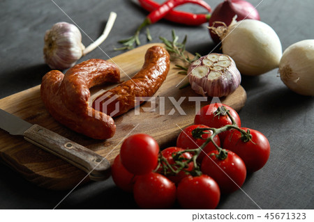 delicious sausages with different vegetables on a wooden board, knife on a black table 45671323