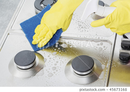 Hands in yellow gloves washing the gas stove. Hands in yellow gloves washing the gas stove. 45673168