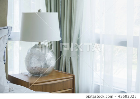 Reading lamp on night table next to window Reading lamp on night table next to window 45692325