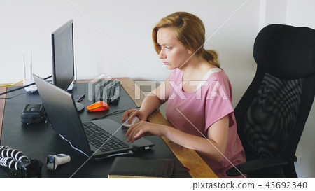 beautiful young woman working on a laptop and computer while sitting at a desk. beautiful young woman working on a laptop and computer while sitting at a desk. 45692340