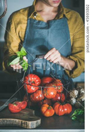 Woman in apron holding basket with heirloom tomatoes for cooking Woman in apron holding basket with heirloom tomatoes for cooking 45693802