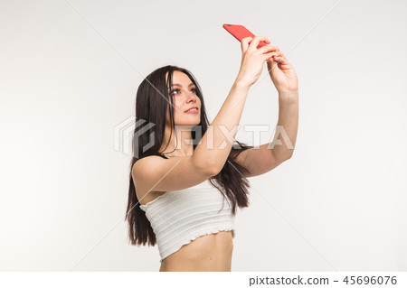 Technology and people concept - young woman making a selfie photo and smiling on white background Technology and people concept - young woman making a selfie photo and smiling on white background 45696076