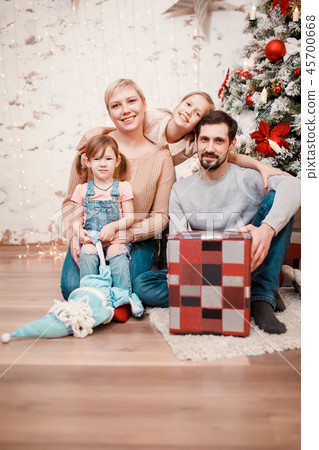 Photo of happy family sitting with box with gift at decorated New Year tree Photo of happy family sitting with box with gift at decorated New Year tree 45700668