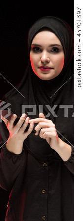 Portrait of beautiful positive friendly young muslim woman wearing black hijab holding mobile phone Portrait of beautiful positive friendly young muslim woman wearing black hijab holding mobile phone 45701397