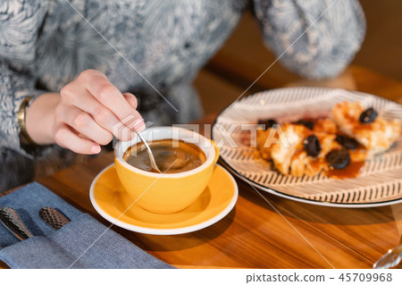 Young woman drinking coffee. Female holding cup. Sitting in coffee shop at wooden table. On table Young woman drinking coffee. Female holding cup. Sitting in coffee shop at wooden table. On table 45709968