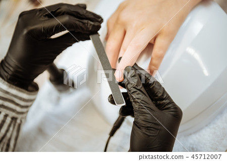 Close up of professional nail artist wearing black gloves holding nail file 45712007