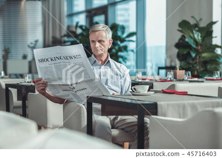 Serious mature man reading newspaper in the cafe Serious mature man reading newspaper in the cafe 45716403