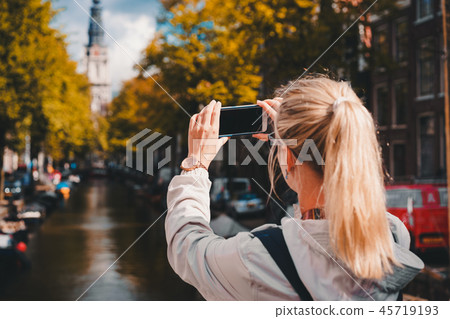 Woman tourist taking a picture of canal in Amsterdam on the mobile phone. Warm gold afternoon Woman tourist taking a picture of canal in Amsterdam on the mobile phone. Warm gold afternoon 45719193