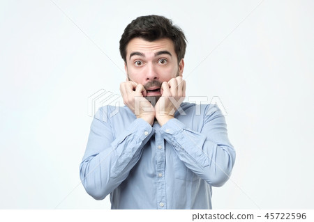 Young man dressed in casual clothes, biting nails and rounding eyes Young man dressed in casual clothes, biting nails and rounding eyes 45722596