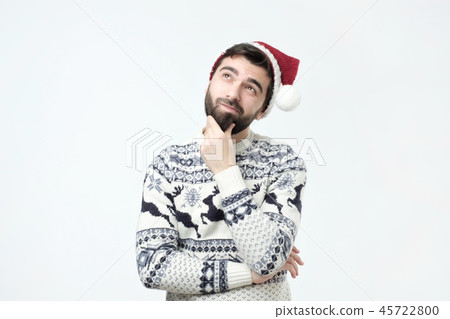 Hispanic man in red christmas cap thinking deeply about gifts, looking up. 45722800