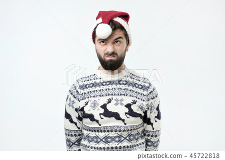 Man in red christmas hat frowns face with displeasure, has irritated expression, being discontent. Man in red christmas hat frowns face with displeasure, has irritated expression, being discontent. 45722818