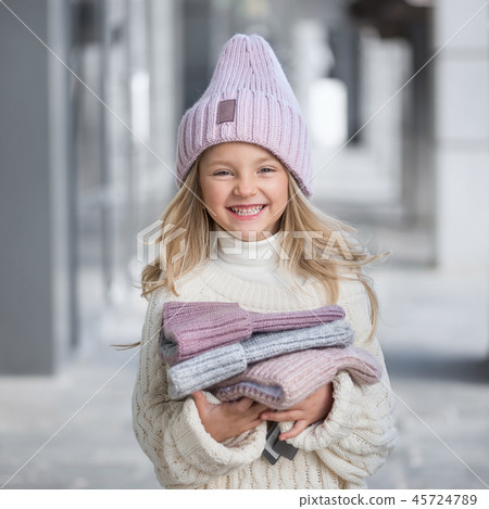Cute little girl in a knitted lilac hat holding a new knitted hats 45724789