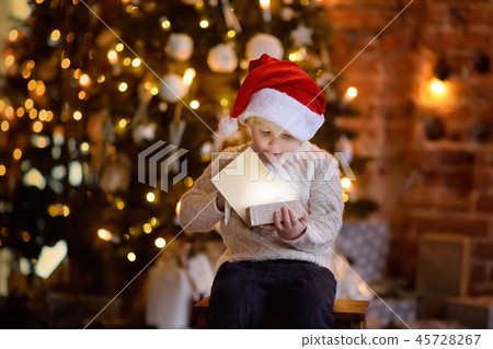 Boy wearing Santa hat opening a Christmas gift 45728267