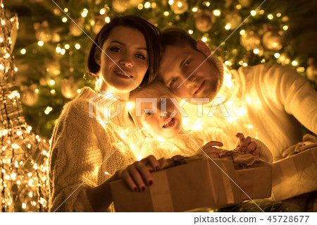 Happy family wrapped in a garland sits near a Christmas tree. New year. Happy family wrapped in a garland sits near a Christmas tree. New year. 45728677
