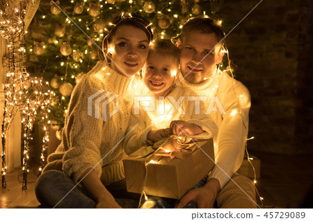 Happy family wrapped in a garland sits near a Christmas tree. Happy family wrapped in a garland sits near a Christmas tree. 45729089