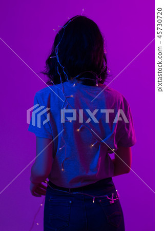 Portrait of young woman with hanging christmas lights on her body Portrait of young woman with hanging christmas lights on her body 45730720