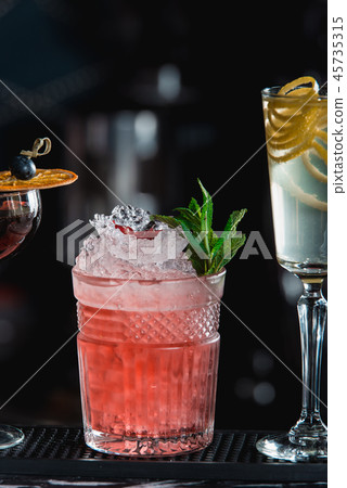 Cold cocktail with ice and garnet seeds, piece of pomegranate behind on dark background Cold cocktail with ice and garnet seeds, piece of pomegranate behind on dark background 45735315