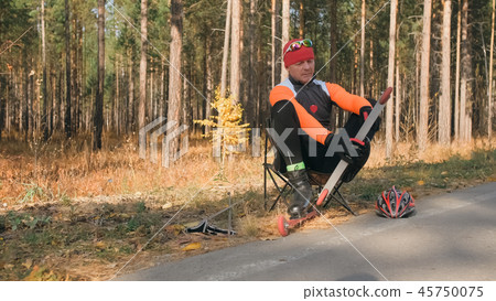 Training an athlete on the roller skaters. Biathlon ride on the roller skis with ski poles, in the 45750075