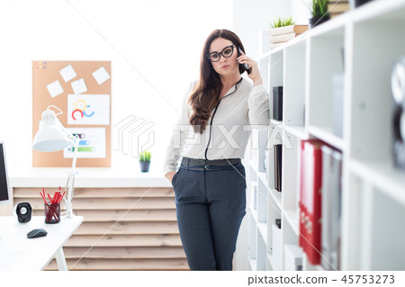 A young girl standing near the rack with documents and holding a phone. 45753273