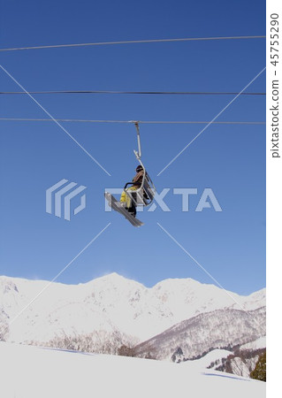 A ski lift in Hakuba-mura, Nagano Prefecture, carrying a snowboarder against the backdrop of a sunny Northern Alps Hakuba Sanzan 45755290