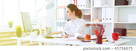 A young girl in the office holds a pink marker in her hand and works with a computer and documents. 45756075
