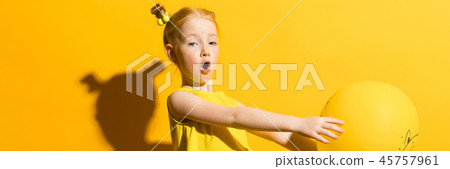 Girl with red hair on a yellow background. The girl is holding a yellow balloon on her outstretched Girl with red hair on a yellow background. The girl is holding a yellow balloon on her outstretched 45757961