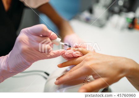 Beautician applying nail varnish to female client Beautician applying nail varnish to female client 45760960