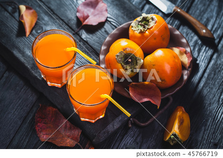 Ripe orange persimmon fruit and persimmon leaves in a brown plate on a black wooden table Ripe orange persimmon fruit and persimmon leaves in a brown plate on a black wooden table 45766719