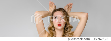 A young beautiful girl fools by putting two hands on her head and twisting her face. Funny portrait A young beautiful girl fools by putting two hands on her head and twisting her face. Funny portrait 45767328