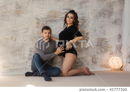 Happy man put his handr on the belly of his pregnant wife. Young family in studio. Couple wait for a Happy man put his handr on the belly of his pregnant wife. Young family in studio. Couple wait for a 45777300